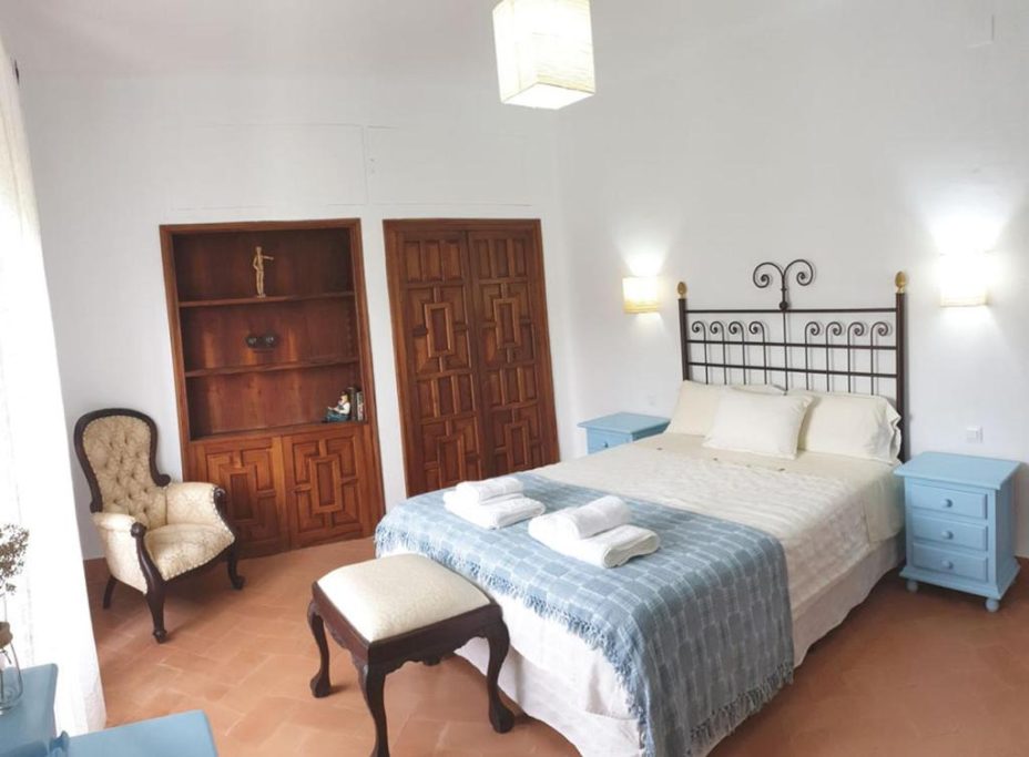 Habitación luminosa con cama doble, muebles de madera y silla decorativa.