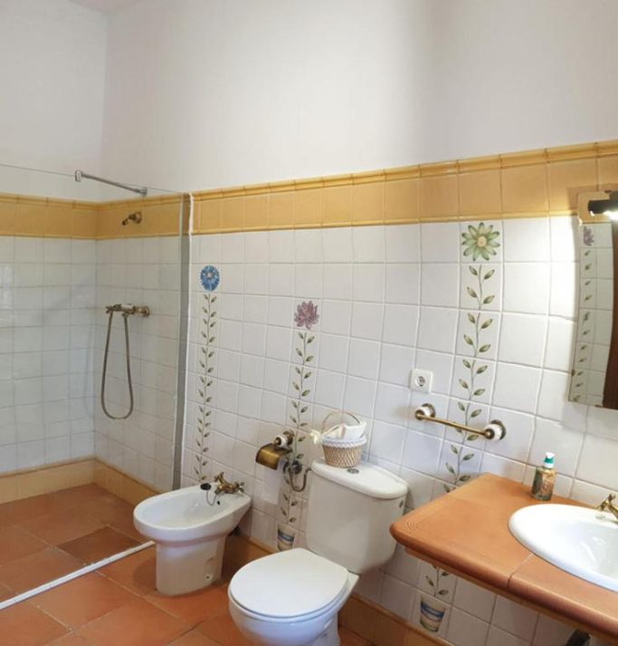 Baño con ducha, inodoro, bidé y lavabo en azulejos claros con decoración floral.