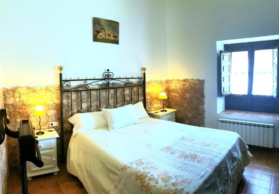 Habitación acogedora con cama doble, mesitas de noche y ventanales iluminados.