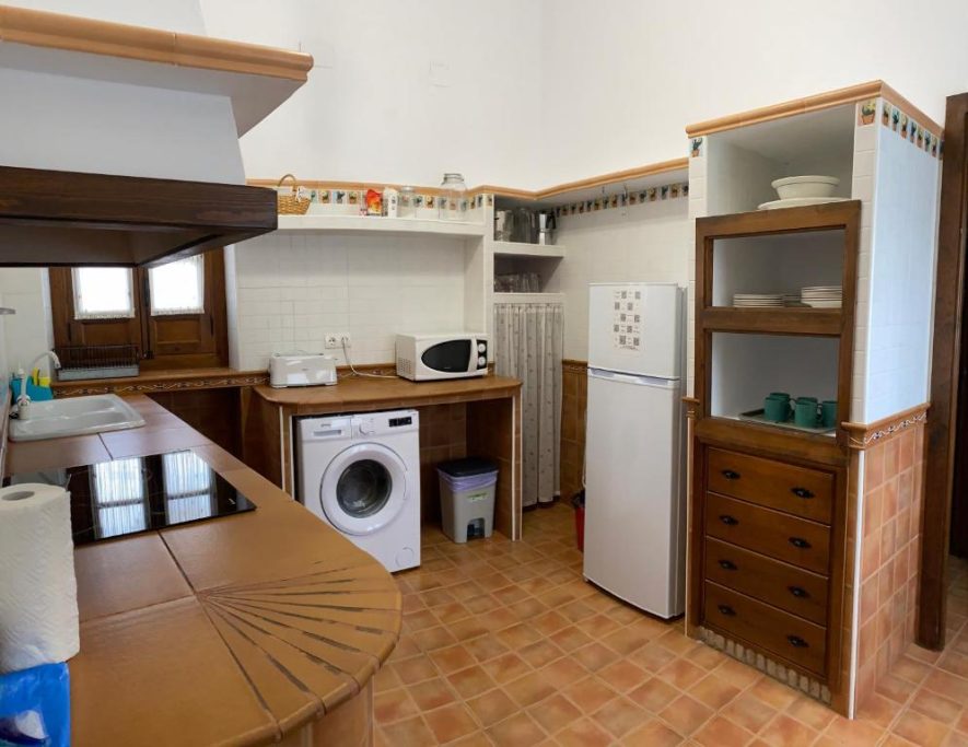 Cocina moderna con nevera, lavadora y microondas, muebles de madera claros.