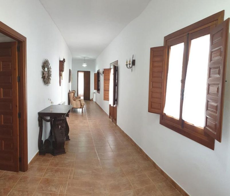 Pasillo luminoso con ventanas de madera y muebles sencillos a los lados.