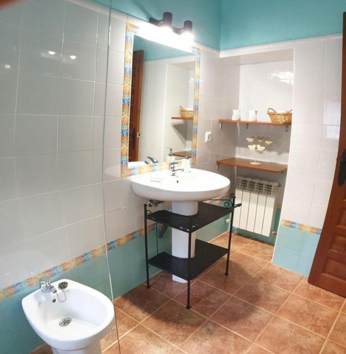 Baño moderno con lavabo, espejo, estanterías y azulejos en tonos aqua y terracota.