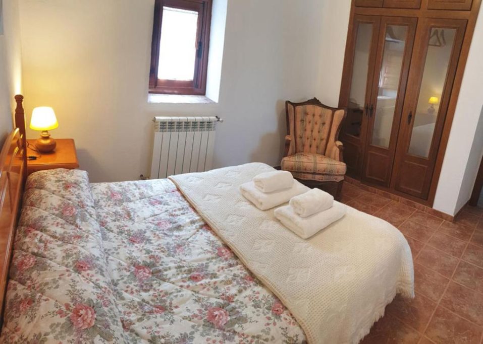 Habitación luminosa con cama matrimonial, silla decorativa y armario de madera.