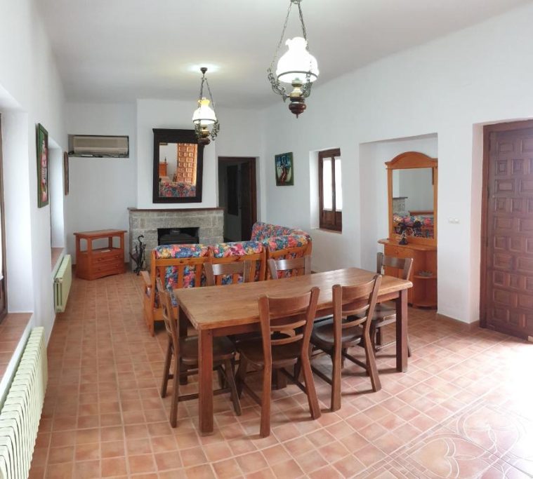 Sala de estar con sofá colorido, mesa de comedor y lámparas colgantes.